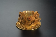 Leisi Filigree Bun—Net with Two Dragons
Ming dynasty (1368–1644)
Diameter 9.6 cm, Height 6.4 cm, Weight 138.5 g (inlays included)
Mengdiexuan collection
The underlying shape of this hair ornament is made of filigree, and consists of a hemispherical, ribbed top attached to a round, flat, collar-like base. The top and base are joined with gold foil, while the standing wing-shaped ornaments at the sides and back are attached to the base with hooks. Holes on the sides of the base enabled the whole accessory to be secured to the head. The ornament is elaborately decorated. Bats and lotus flowers decorate the top and the collar below. The wing-shaped ornaments are embellished with five-clawed dragons chasing an inlaid flaming red gemstone amidst cloud scrolls. The dragons’ necks are made of springs so that their heads would sway with movement.